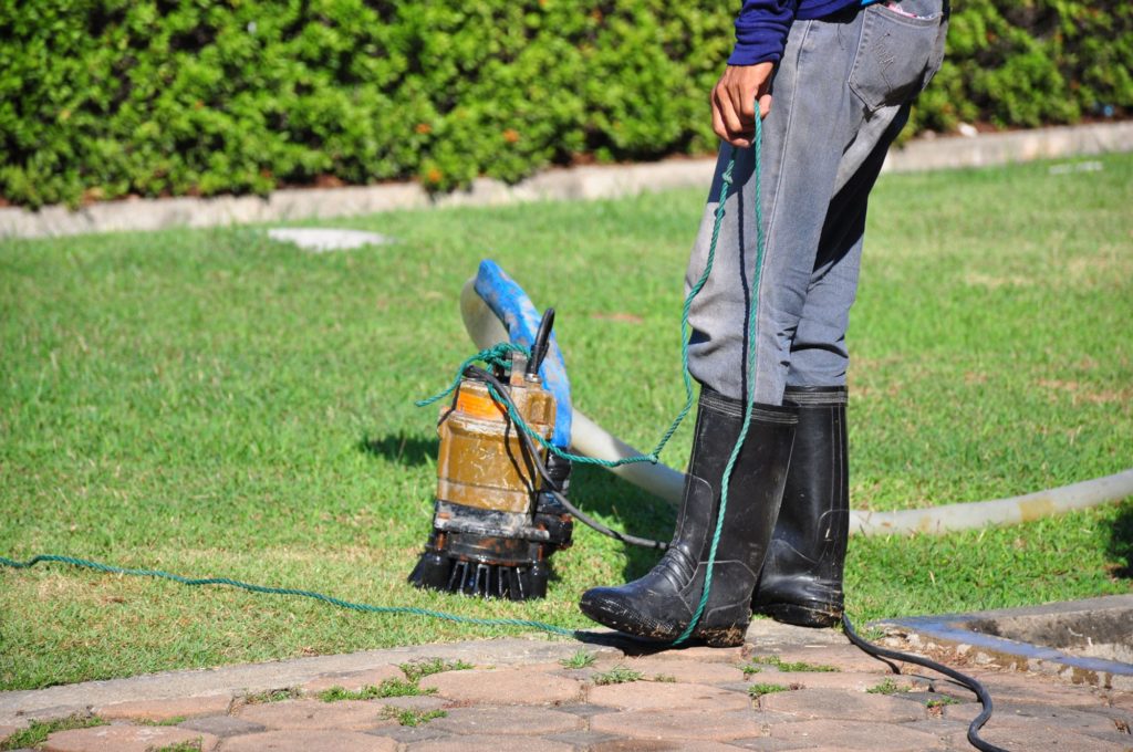 Homeowner wearing boots looking at sump pump on lawn