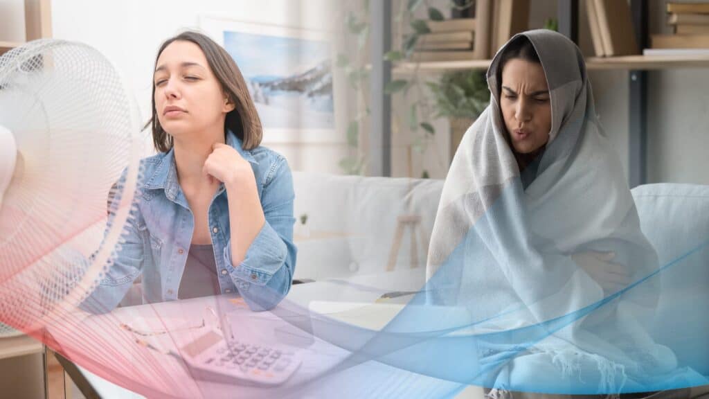 Two women sit on a couch; one cools herself in front of a fan while the other, wrapped in a blanket, shivers—showing just how noticeable temperature imbalance can be at home.