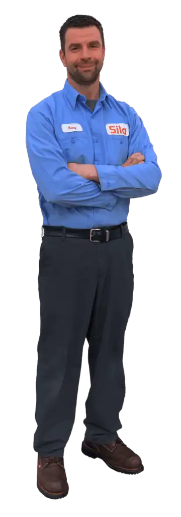 A man wearing a blue button-up shirt with a "Sila" logo and dark pants stands with arms crossed, facing forward.