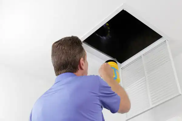 A person holding a flashlight inspects an open ceiling air vent during an Air Duct Repair in White Plains, NY.