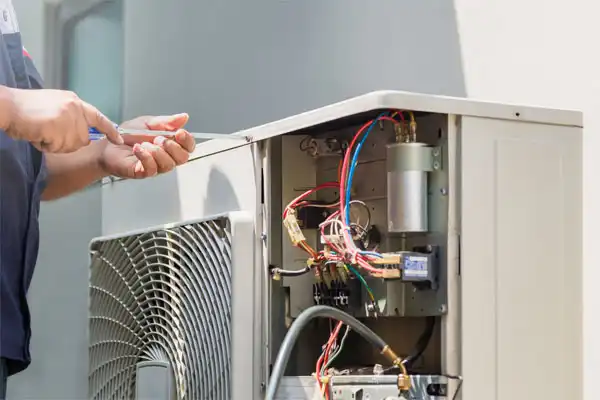 Technician using a screwdriver to repair or maintain an open outdoor air conditioning unit with exposed wires and components in White Plains, NY.