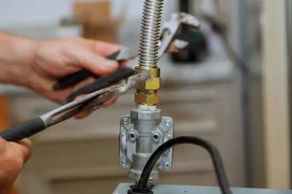 Close-up of hands using pliers to tighten a gas pipe fitting on a metal valve during a gas line installation in White Plains, NY, with a flexible connector and tools visible.