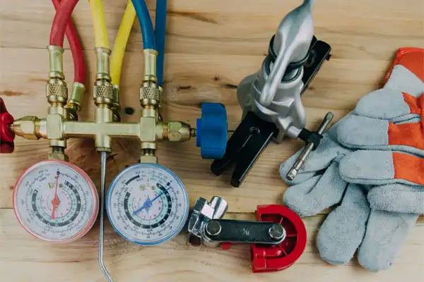Manifold gauge set, pipe cutter, gloves, and other essential HVAC tools for heating installation neatly arranged on a wooden surface.