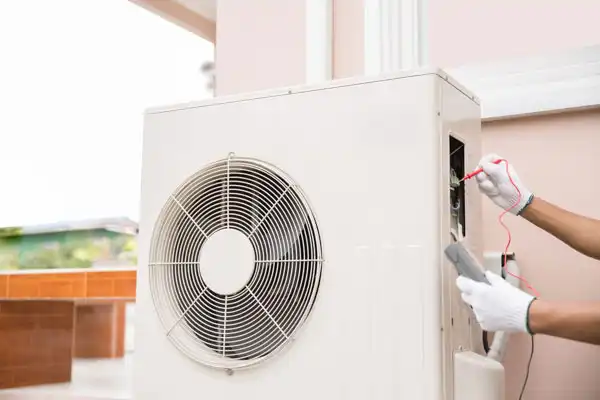 A person wearing white gloves uses a multimeter to check an outdoor air conditioning unit during heat pump maintenance in White Plains, NY.