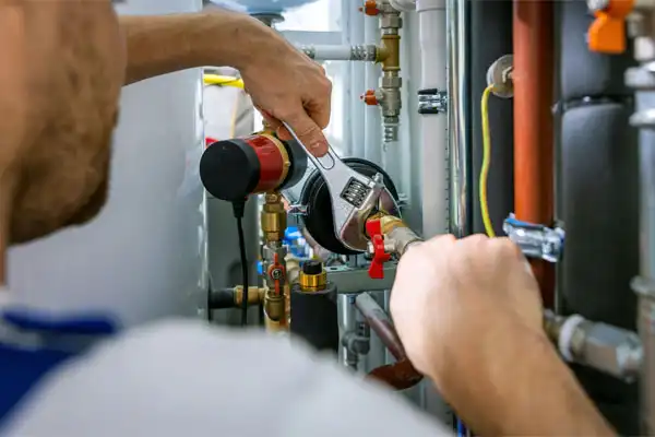 A person uses a wrench to adjust plumbing pipes and valves during a humidifier installation in a utility room in White Plains, NY.