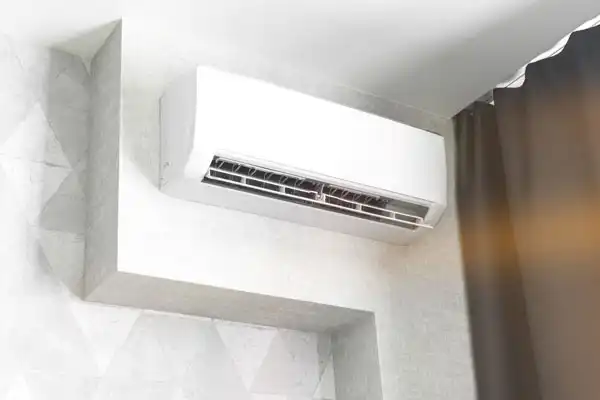 A white wall-mounted air conditioner, ideal for mini-split repair in White Plains, NY, is installed above a window near dark curtains in a modern room with light-colored walls.