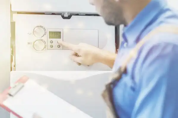 A person in a blue shirt adjusts the settings on a boiler control panel while holding a clipboard, overseeing a tankless water heater installation in White Plains, NY.