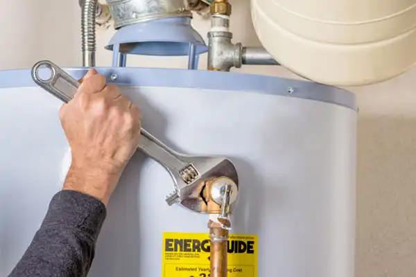 A person performs water heater repair in White Plains NY, using a large adjustable wrench to tighten a pipe fitting on a tank with an EnergyGuide label.
