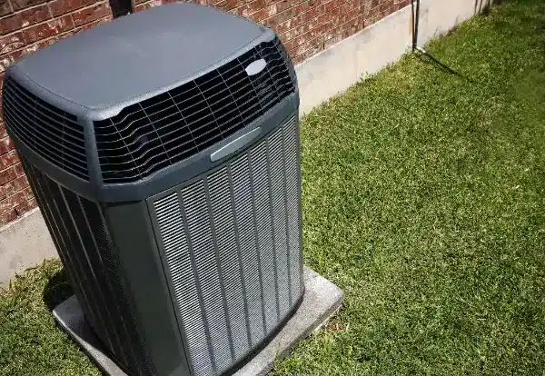 An outdoor air conditioning unit is installed on a concrete pad next to a brick wall, surrounded by grass, showcasing professional Air Conditioning Installation in White Plains, NY.