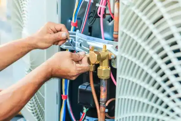 A person performs Air Conditioning Maintenance on an HVAC unit in White Plains, NY, adjusting wires and valves amid various colored cables and metal components.