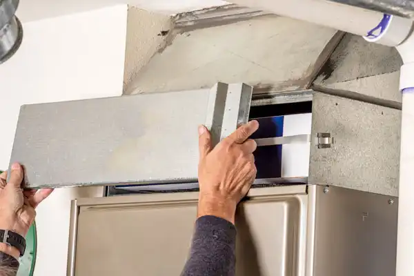 A person in White Plains, NY removes the cover of a furnace to access the air filter inside as part of routine furnace maintenance.